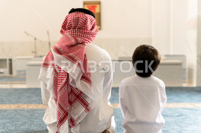 Teaching the performance of the obligatory prayer for a child inside the mosque, a Saudi man prays in the chapel next to his adult son, reverence in the prayer, performing the obligatory prayer in the mosque, worship and drawing closer to God, teaching pr