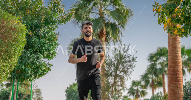 المنتزهات والحدائق العامة، ممارسة رياضة المشي، النباتات الخضراء والأشجار، رجل عربي خليجي سعودي مبتسم يقوم بالتمارين الصباحية، الصحه واللياقه الجسديه، نشاط بدني في الهواء الطلق، ايماءات السعادة والسرور