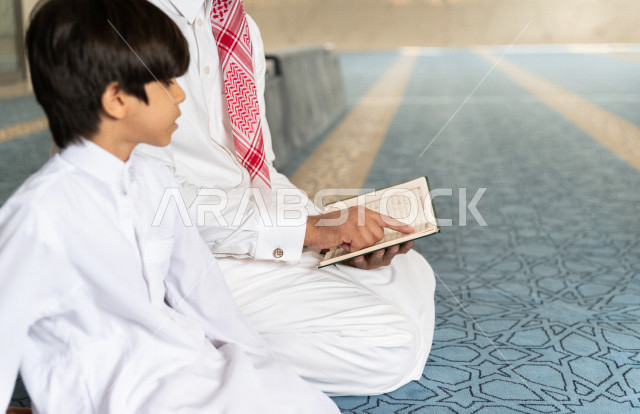 رجل سعودي مسلم يجلس داخل المسجد و بجانبه طفل صغير ، يقرآن القرآن الكريم ، تحفيظ القرأن الكريم  للأطفال ، تلاوة القرآن الكريم ، العبادة و التقرب الى الله