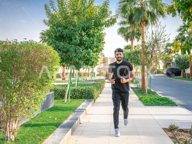 الأشجار والنباتات الخضراء، التنزه في الحدائق العامة، نشاط بدني في الهواء الطلق، ممارسة رياضة المشي في ممشى المنتزه، الصحه واللياقه الجسديه، رجل عربي خليجي سعودي يقوم بالتمارين الصباحية، صورة لكامل الجسم