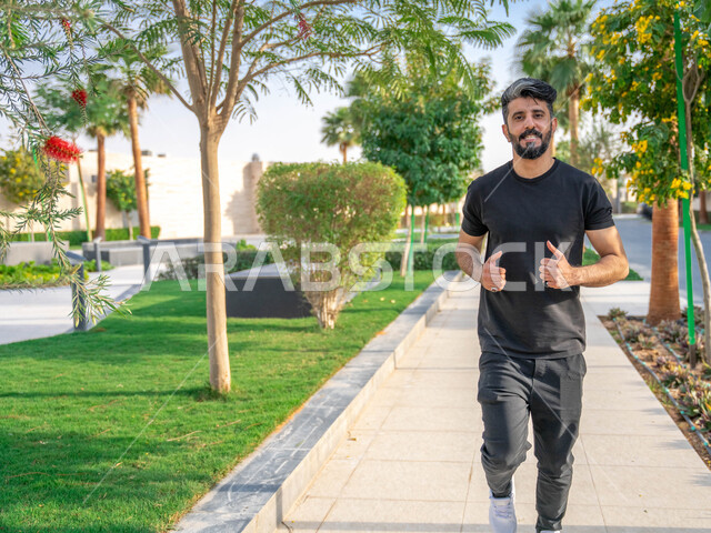 الأشجار والنباتات الخضراء، التنزه في الحدائق العامة، نشاط بدني في الهواء الطلق، ممارسة رياضة المشي في ممشى المنتزه، الصحه واللياقه الجسديه، رجل عربي خليجي سعودي يقوم بالتمارين الصباحية، صورة لكامل الجسم