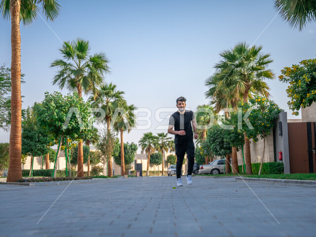 نشاط بدني في الهواء الطلق، ممارسة رياضة المشي في ممشى المنتزه، الصحه واللياقه الجسديه، رجل عربي خليجي سعودي يقوم بالتمارين الصباحية، التنزه في الحدائق العامة، الأشجار والنباتات الخضراء، صورة لكامل الجسم
