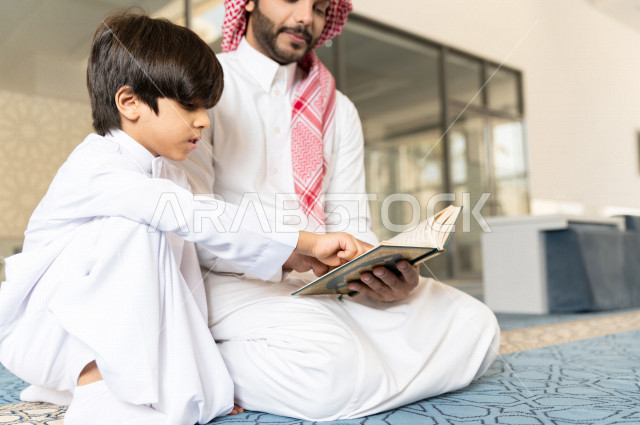 رجل سعودي مسلم يجلس داخل المسجد و بجانبه طفل صغير ، يقرآن القرآن الكريم ، تحفيظ القرأن الكريم  للأطفال ، تلاوة القرآن الكريم ، العبادة و التقرب الى الله