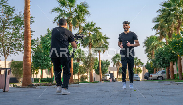 ممارسة التمارين الرياضيه للحفاظ على الرشاقه والنشاط البدني، جلسة تصوير في احدى الحدائق للعامه، مصور عربي خليجي سعودي يقوم بتصوير شاب يمارس رياضة الجري في الهواء الطلق، خلفية الطبيعه