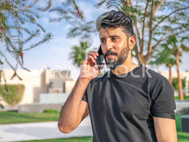 اجراء مكالمات الهاتفية اثناء ممارسة رياضة المشي، تبادل الاحاديث المضحكة والمسلية عبرالموبايل، المنتزهات والحدائق العامة، الدردشة والتواصل مع الأهل والاصدقاء، صورة مقربة لرجل عربي خليجي سعودي مبتسم يقوم بالتمارين الصباحية، نشاط بدني في الهواء الطلق