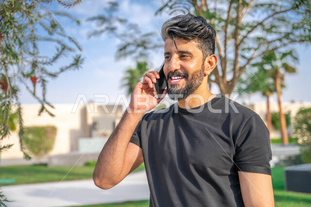 نشاط بدني في الهواء الطلق، اجراء مكالمات الهاتفية اثناء ممارسة رياضة المشي، تبادل الاحاديث المضحكة والمسلية عبرالموبايل، المنتزهات والحدائق العامة، الدردشة والتواصل مع الأهل والاصدقاء، صورة مقربة لرجل عربي خليجي سعودي مبتسم يقوم بالتمارين الصباحية