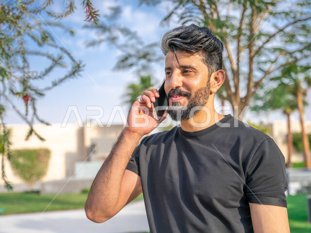 الصحه واللياقه الجسديه، اجراء مكالمات الهاتفية اثناء ممارسة رياضة المشي، تبادل الاحاديث المضحكة والمسلية عبرالموبايل، المنتزهات والحدائق العامة، الدردشة والتواصل مع الأهل والاصدقاء، صورة مقربة لرجل عربي خليجي سعودي مبتسم يقوم بالتمارين الصباحية