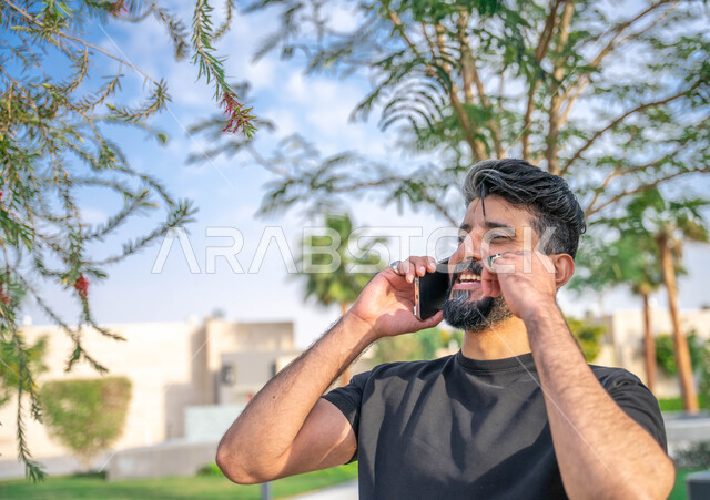 ايماءات الضحك الشديد، اجراء مكالمات الهاتفية اثناء ممارسة رياضة المشي، تبادل الاحاديث المضحكة والمسلية عبرالموبايل، المنتزهات والحدائق العامة، الدردشة والتواصل مع الأهل والاصدقاء، صورة مقربة لرجل عربي خليجي سعودي مبتسم يقوم بالتمارين الصباحية