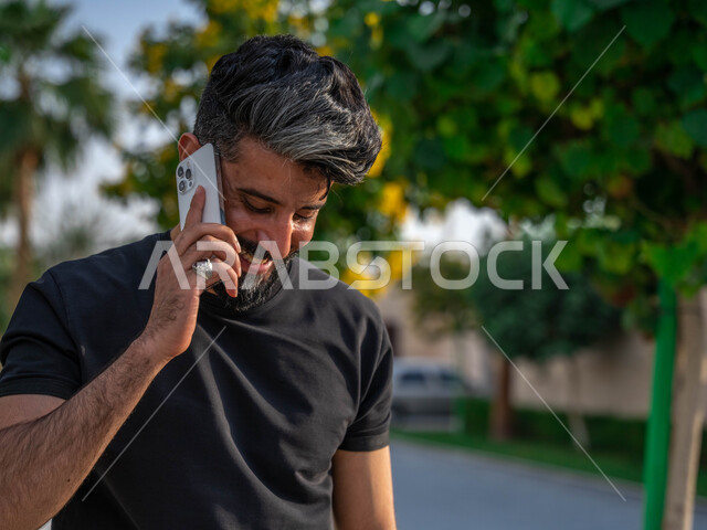 ايماءات الخجل والحياء، اجراء مكالمات الهاتفية اثناء ممارسة رياضة المشي، تبادل الاحاديث المضحكة والمسلية عبرالموبايل، المنتزهات والحدائق العامة، الدردشة والتواصل مع الأهل والاصدقاء، صورة مقربة لرجل عربي خليجي سعودي مبتسم يقوم بالتمارين الصباحية