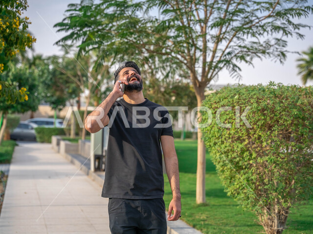 ايماءات الضحك الشديد، اجراء مكالمات الهاتفية اثناء ممارسة رياضة المشي، تبادل الاحاديث المضحكة والمسلية عبرالموبايل، المنتزهات والحدائق العامة، الدردشة والتواصل مع الأهل والاصدقاء، صورة مقربة لرجل عربي خليجي سعودي مبتسم يقوم بالتمارين الصباحية