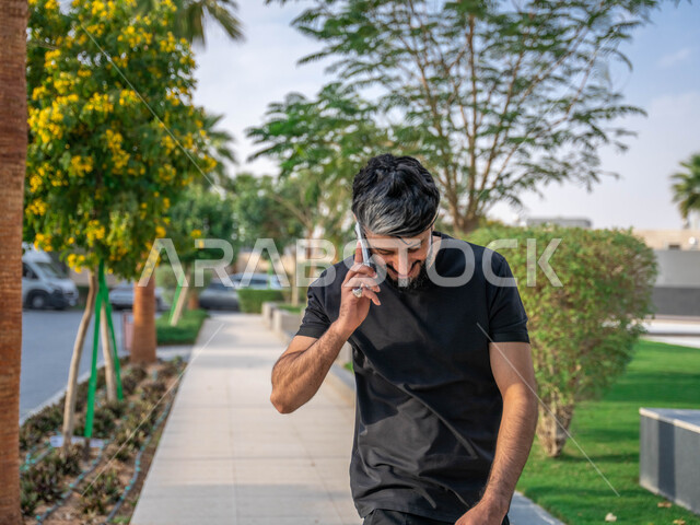 تعابير الضحك الشديد، اجراء مكالمات الهاتفية اثناء ممارسة رياضة المشي، تبادل الاحاديث المضحكة والمسلية عبرالموبايل، المنتزهات والحدائق العامة، الدردشة والتواصل مع الأهل والاصدقاء، صورة مقربة لرجل عربي خليجي سعودي مبتسم يقوم بالتمارين الصباحية
