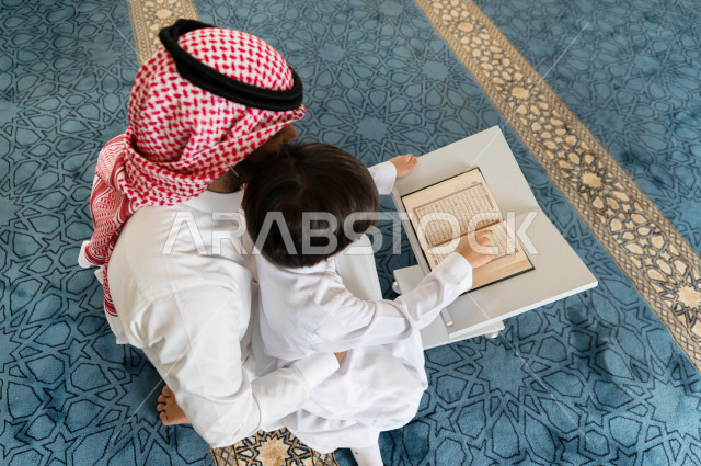 رجل سعودي مسلم يجلس داخل المسجد و بجانبه طفل صغير ، يقرآن القرآن الكريم ، تحفيظ القرأن الكريم  للأطفال ، تلاوة القرآن الكريم ، العبادة و التقرب الى الله