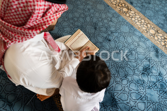 رجل سعودي مسلم يجلس داخل المسجد و بجانبه طفل صغير ، يقرآن القرآن الكريم ، تحفيظ القرأن الكريم  للأطفال ، تلاوة القرآن الكريم ، العبادة و التقرب الى الله