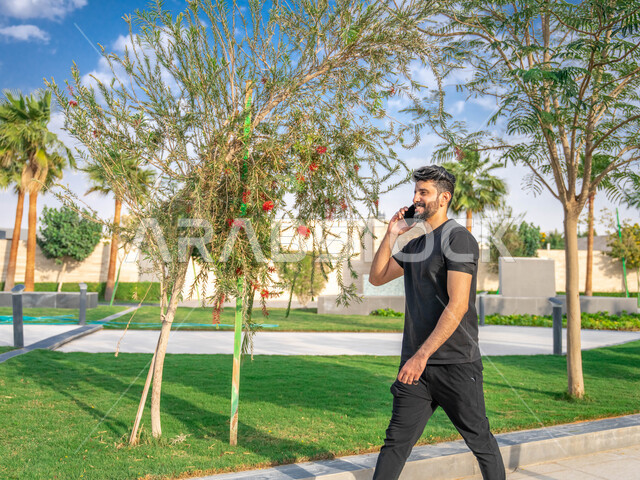 الحفاظ على الرشاقه والنشاط البدني، ، تبادل الاحاديث المضحكة والمسلية عبرالموبايل، المنتزهات والحدائق العامة، الدردشة والتواصل مع الأهل والاصدقاء، رجل عربي خليجي سعودي مبتسم، نشاط بدني في الهواء الطلق، اجراء مكالمات الهاتفية اثناء ممارسة التمارين الرياضيه