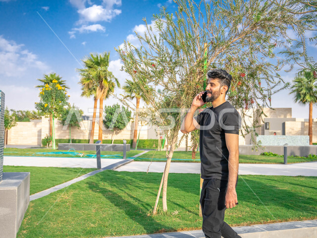 الدردشة والتواصل مع الأهل والاصدقاء، رجل عربي خليجي سعودي مبتسم، نشاط بدني في الهواء الطلق، اجراء مكالمات الهاتفية اثناء ممارسة التمارين الرياضيه، الحفاظ على الرشاقه والنشاط البدني، تبادل الاحاديث المضحكة والمسلية عبر الموبايل، المنتزهات والحدائق العامة