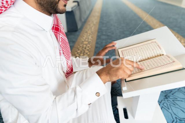 رجل سعودي مسلم يجلس داخل المسجد و يقرأ القرآن الموضوع على كرسي المصحف ، تحفيظ القرأن ، تلاوة القرآن الكريم ، العبادة و التقرب الى الله