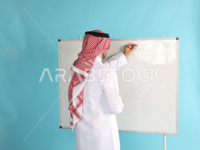 Holding training courses in Saudi Arabia, a close-up portrait from the back of a Saudi Gulf Arab man wearing a shemagh and traditional dress, writing on the blackboard, the profession of a teacher in schools and educational institutes, writing on a white board, blue background