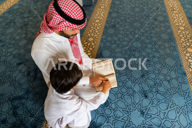 رجل سعودي مسلم يجلس داخل المسجد و بجانبه طفل صغير ، يقرآن القرآن الكريم ، تحفيظ القرأن الكريم  للأطفال ، تلاوة القرآن الكريم ، العبادة و التقرب الى الله