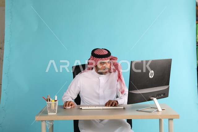مهن ووظائف مكتبية سعودية، مفهوم ادارة الاعمال وتحقيق اهداف الشركة، بورتريه لرجل اعمال عربي خليجي سعودي يرتدي الشماغ والثوب التقليدي يجلس في مكتبه يعمل على الحاسوب المحمول بايماءات الحماس والسعادة، انجاز مهام العمل عن بعد، خلفية زرقاء