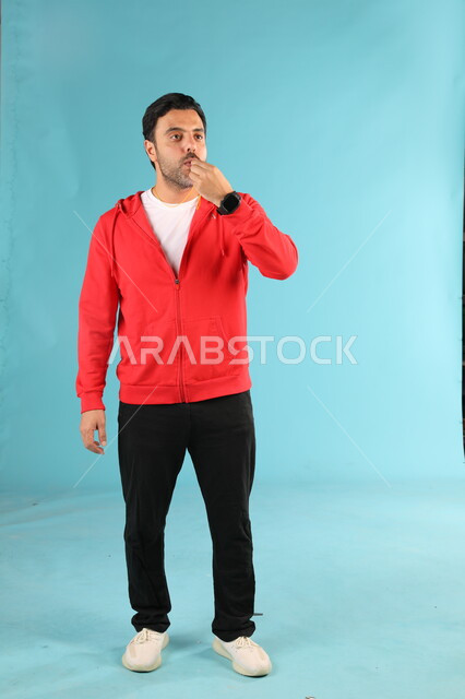 استخدام الصفارة للتنبيه والتحذير، الوقوف باستقامة والنظر الى شيء ما، الرياضات السعودية الشبابية، ممارسة الهوايات الرياضية، بورتريه لمدرب عربي خليجي سعودي يرتدي الملابس الرياضية يقوم بالتصفير، صورة الجسم بالطول الكامل، خلفية زرقاء