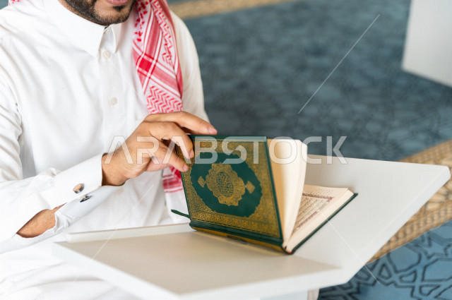 رجل سعودي مسلم يجلس داخل المسجد و يقرأ القرآن الموضوع على كرسي المصحف ، تحفيظ القرأن ، تلاوة القرآن الكريم ، العبادة و التقرب الى الله