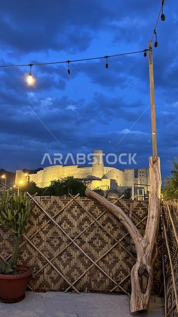 معلم عسكري تاريخي اثري, منظر السماء الملبدة بالغيوم في الليل, اطلالة سطح منزل على قلعة بهلاء عبري المبنية من الطين في سلطنة عمان, التصميم والفن الهندسي المعماري على الطراز الهندسي القديم، معالم سياحيه تراثيه مشهورة