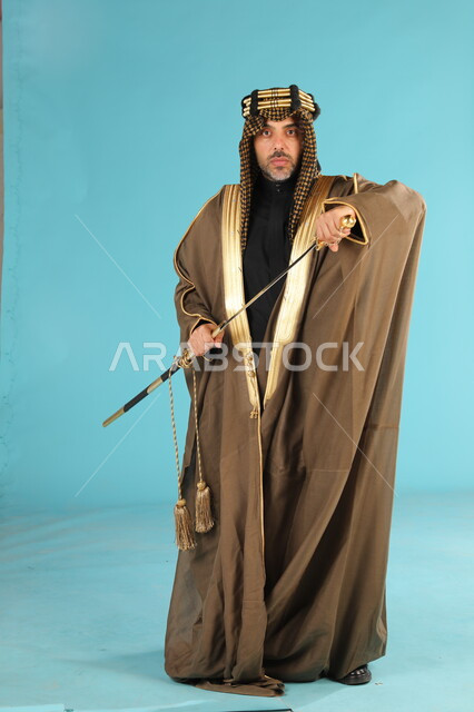 Anniversary of the founding of the first Saudi state on February 22, Day of Badina 1727 AD, portrait of a Saudi Gulf Arab man wearing a bisht and golden headband, holding a sword in his hand and looking at the camera with proud gestures, adhering to the Gulf heritage, full body portrait, blue background