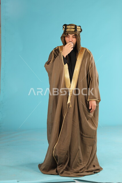 الاستمتاع بالمشروبات الساخنة، فخر المنتجات المحلية، يوم بدينا 1727م، ذكرى تأسيس الدولة السعودية الأولى في 22فبراير، بورتريه لرجل عربي خليجي سعودي يرتدي البشت والعقال الذهبي يشرب القهوة العربية، صورة الجسم بالكامل، خلفية زرقاء