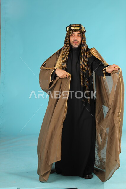 Anniversary of the founding of the first Saudi state on February 22, the Day of Badina 1727 AD, portrait of a Saudi Gulf Arab man wearing a bisht and golden headband looking at the camera, pride and bragging about the country’s achievements, full body portrait, blue background