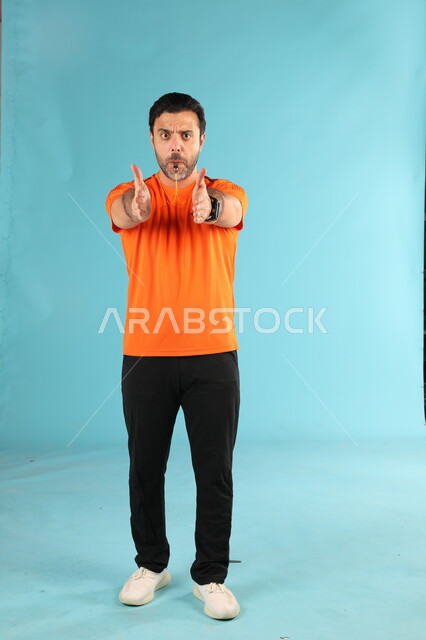 الرياضات السعودية الشبابية, ممارسة الهوايات الممتعه، استخدام الصفارة للتنبيه والتحذير، بورتريه لمدرب عربي خليجي سعودي يرتدي الملابس الرياضية يقوم بالتصفير يرفع يديه بطلب التقدم والاستمرار باللعب، صورة الجسم بالطول الكامل، خلفية زرقاء