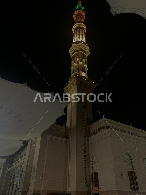 صورة مقربة لإحدى مآذن المسجد النبوي الشريف في الليل، المظلات الالكترونية في ساحة الحرم النبوي في المدينة المنورة، العبادة والتقرب الى الله، أماكن إسلامية دينية مقدسة في المملكة العربية السعودية