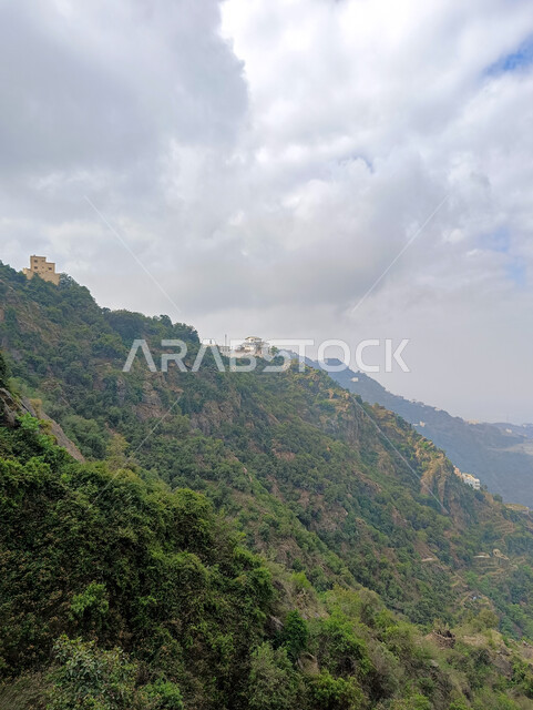 السماء المليئة بالغيوم البيضاء فوق سفوح الجبال، الأشجار والنباتات الخضراء، المعالم الاثرية التاريخية على القمم والمرتفعات الجبلية في مدينة جازان، المباني القديمة في محافظة فيفاء في المملكة العربية السعودية، خلفية الطبيعة