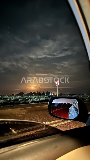 A picture from inside the car of the view of the clouds and the Milky Way in the sky, asphalt roads and streets at night, tourist areas and night tours in the Kingdom of Saudi Arabia