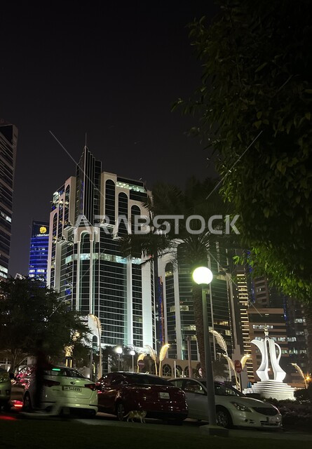 Residential and commercial towers and facilities illuminated at night on the Doha Corniche, the economic and urban renaissance of the city of Doha, advanced architectural engineering, famous landmarks and places in the State of Qatar, interest in planting trees and green plants in tourist cities.