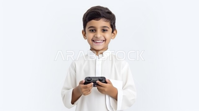 الاستمتاع بالتقنيات والتكنولوجيا الحديثة، قضاء وقت ممتع بعلب ألعاب الفيديو، مفهوم المتعة والتسلية، برامج الكمبيوتر الترفيهية، بورتريه مقرب لطفل عربي خليجي سعودي مبتسم يرتدي الثوب التقليدي و يمسك بيده عصا اللعب، خلفية بيضاء
