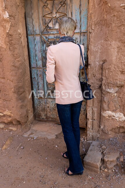 أماكن ومعالم الجذب السياحي من شتى أنحاء العالم, البيوت والمنشآت الطينية, التجول في الأحياء الشعبية الضيقة في السعودية, صورة من الخلف لسائحة غربية تستمتع بالرحلة السياحية في قرية أشيقر التراثية في محافظة شقراء, قضاء الوقت الممتع والتعرف على الحضارات القديمة