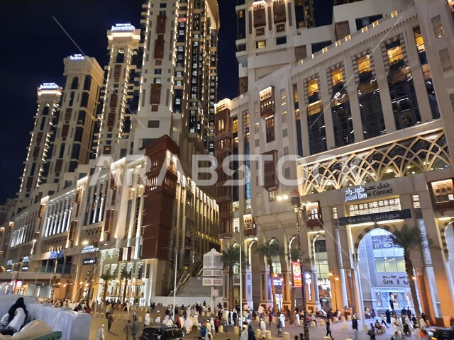 مباني شركة جبل عمر للتطوير العقاري في مكة المكرمة، الفن الهندسي المعماري المتطور للأبراج وناطحات السحاب، فنادق ومنتجعات كونراد الفاخرة المجاورة للمسجد الحرام بالمملكة العربية السعودية، تجمع السياح والحجاج في شارع ابراهيم الخليل في الليل