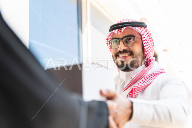 A young Saudi Arabian Gulf man works on delivering orders, delivering boxes and bags containing orders and supplies to a Saudi customer to the door of the house, reliable shipping and delivery, owning a new home, transportation and delivery