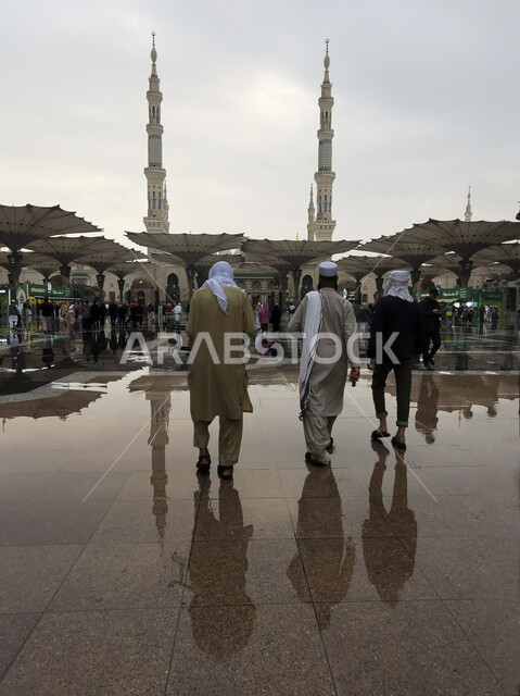 Worshiping and getting closer to God, Muslim pilgrims walking in front of the Prophet’s Mosque in Medina, sacred religious places and landmarks in Saudi Arabia, the reflection of the electronic umbrellas of the courtyards of the Prophet’s Mosque in the rainwater