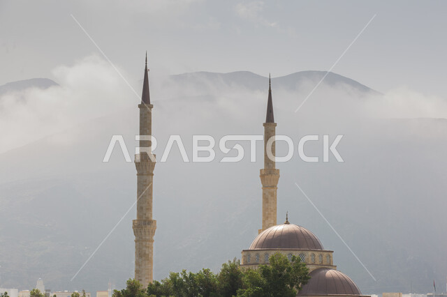 Calling Muslims to pray, worship, and draw closer to God, architectural engineering art in the Islamic style, a close-up of a minaret and the dome of a mosque in the city of Muscat in the Sultanate of Oman, sacred religious tourism places and landmarks, a view of the sky filled with white clouds