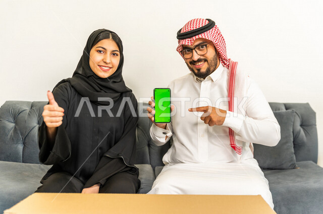 A wonderful atmosphere for a Saudi couple inside their new home, using a mobile phone with a green chrome screen, moving furniture to a new house, owning a new house, unpacking furniture and boxes, arranging and organizing, transporting and delivering
