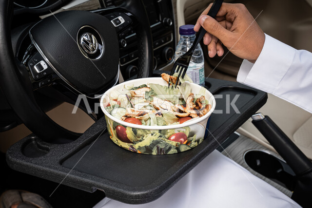 وجبة طعام بسيطه, سناكات صحيه خفيفه, صورة مقربة ليدين شاب عربي خليجي سعودي يرتدي الثوب التقليدي يتناول سلطة السيزر داخل السيارة, مزيج الخضراوات الطازجة والتوست المحمص والدجاج, مأكولات ومقبلات باردة 
