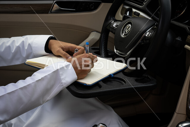 تنظيم وإدارة الأعمال, تدوين وتسجيل الملاحظات والمعلومات على الورق, صورة مقربة ليدين شاب عربي خليجي سعودي يرتدي الثوب التقليدي يجلس داخل السيارة, كتابة المهام والأهداف اليومية
