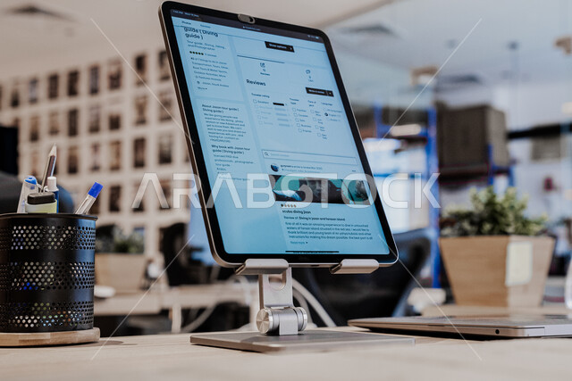 عرض الأجهزة المحمولة في صالات البيع والشراء، التسويق والترويج لمنتجات وطنية محلية سعودية، صورة مقربة لجهاز تابلت محمول على قاعدة في المكتب, نباتات الزينة والأزهار المنزلية، خلفية ضبابية 