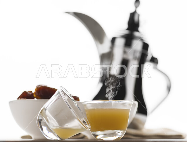 الضيافة وحسن الاستقبال عند العرب, شرب القهوة الخليجية مع حبات من التمر الشهي, منتجات محلية وطنية سعودية, مفهوم إكرام الضيوف, بورتريه لدله قهوة نحاسية فضية مع فنجانين من القهوة السعودية الأصيلة, خلفية بيضاء