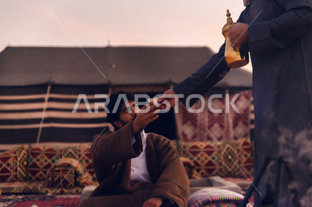 شاب سعودي يقدم القهوه الى صديقه في أجواء صباحيه في صحراء المملكة 