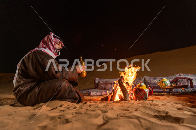 شاب سعودي يصب القهوه العربية في جلسة شعبية , أجواء مسائية في صحراء المملكة 