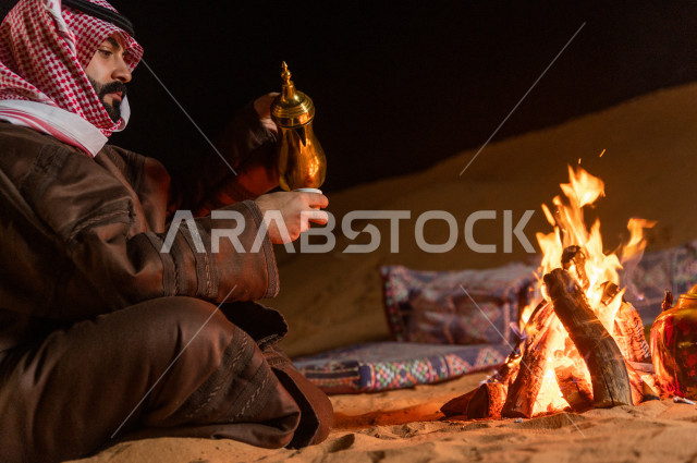 شاب سعودي يصب القهوه العربية في جلسة شعبية , أجواء مسائية في صحراء المملكة 