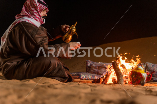شاب سعودي يصب القهوه العربية في جلسة شعبية , أجواء مسائية في صحراء المملكة 