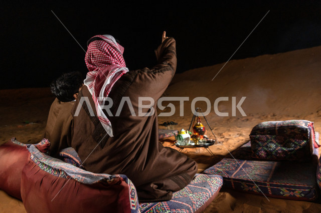 Young Saudis in the evening atmosphere pointing to the sky in the Kingdom's desert, Young Saudis talk and look a the sky in a calm atmosphere in the deserts of Saudi Arabia